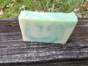 White soap with light green swirls sitting on a ledge with grass and leaves in the background.