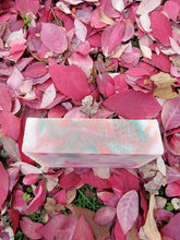 White soap with red and green swirls, green glitter on top sitting in mostly red colored leaves.