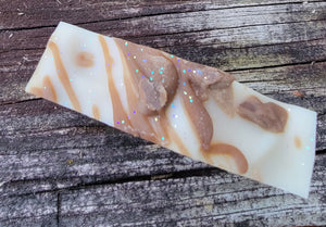 The top of hot chocolate soap which is white with a chocolate drizzle and glitter.  Sitting on a ledge.