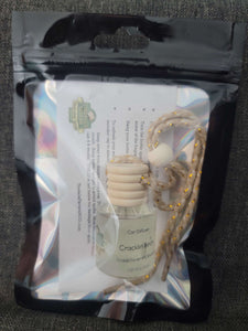 Black holographic mylar bag with instructions inside and a glass car diffuser bottle with a wooden lid and a string to hang it.  Cracklin Birch scent.