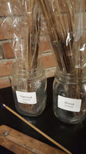 Mason jars with incense sticks sitting inside and one incense stick burning in an incense holder.  Pictured are Patchouli and Wood scents.