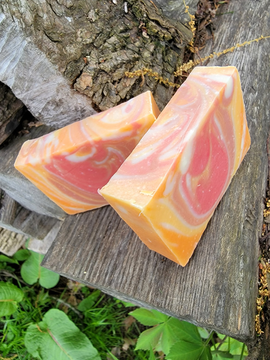 Orange, dark pink and white swirled soap sitting on a piece of wood outside.